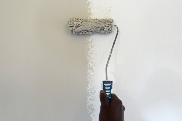 Hand holding paint roller applying fresh white paint to wall